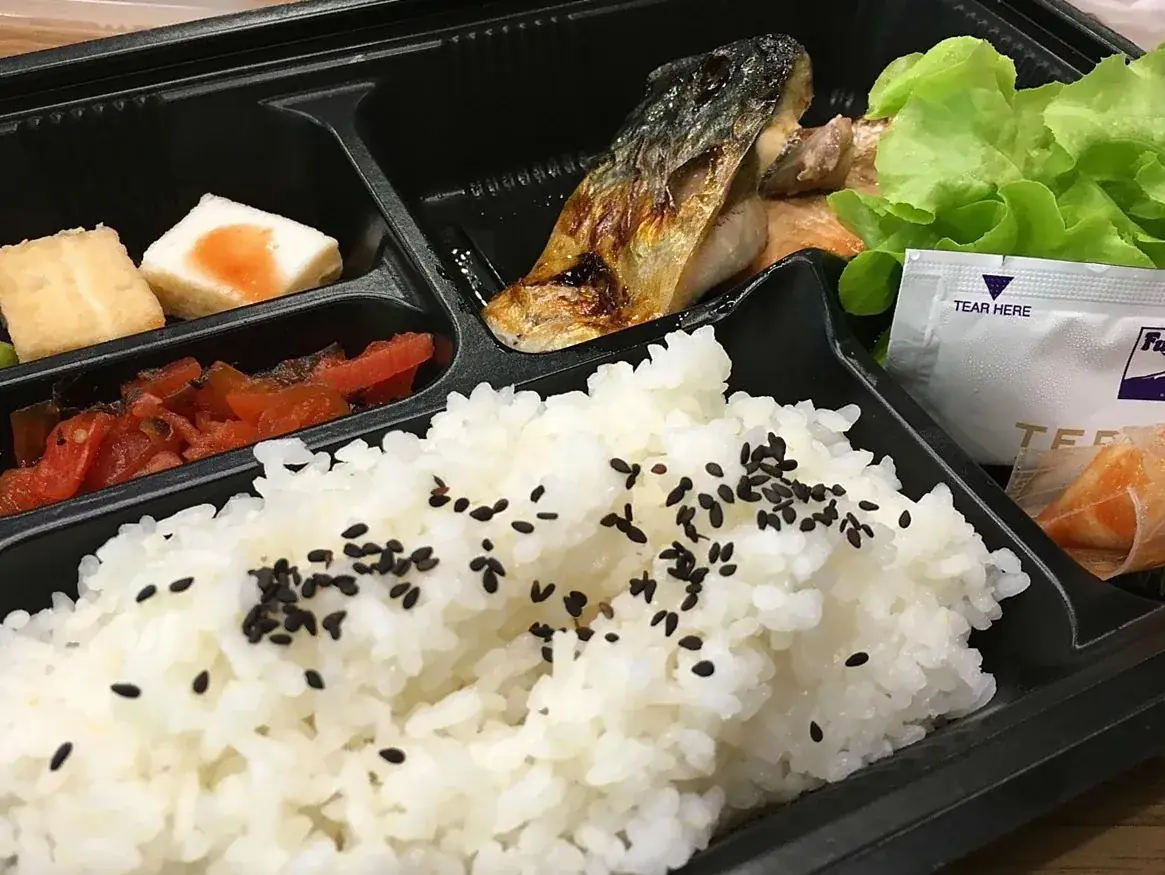 黒ごまをのせたご飯と焼き魚、副菜が入った弁当